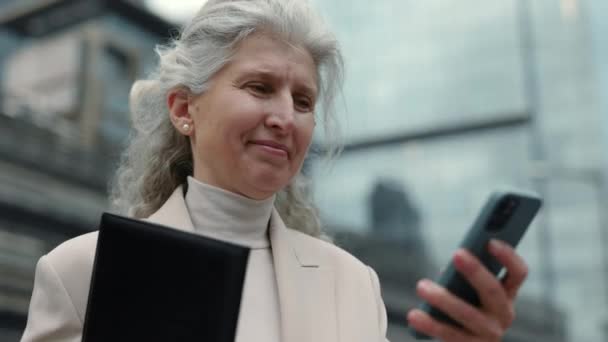 Señora madura usando teléfono inteligente y portapapeles al aire libre — Vídeo de stock