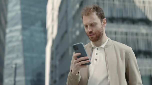 Сфокусированный бизнесмен, стоящий на улице и пользующийся мобильным телефоном — стоковое видео