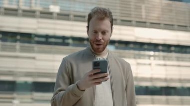 Haberler iyi. Dışarıdaki cep telefonuna bakan şok olmuş bir adam.