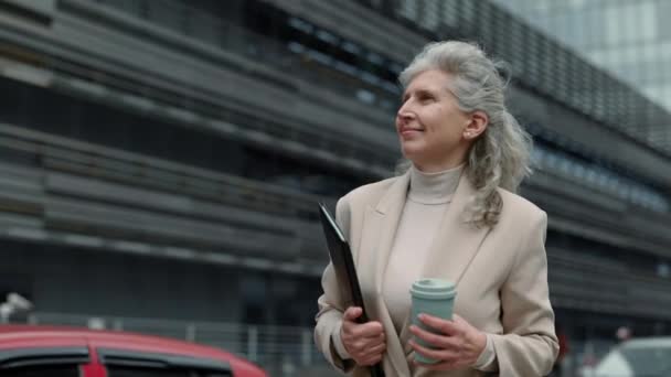Feliz anciana caminando por la calle con portapapeles y café — Vídeo de stock