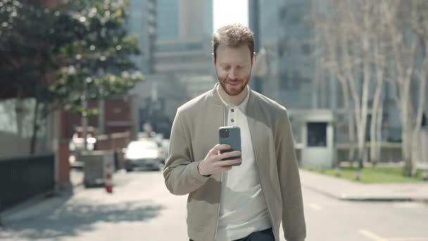 Jeune homme utilisant un smartphone pour discuter en ligne à l'extérieur — Video