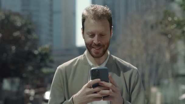 Красавчик ходит по улице и пользуется смартфоном — стоковое видео
