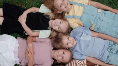 Okul bahçesinde kafa kafaya yatan çok ırklı çocuklar.