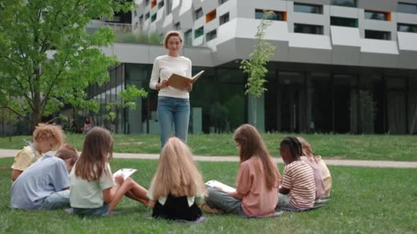 Diverse barn som har undervisning utendørs med en kvinnelig lærer – stockvideo