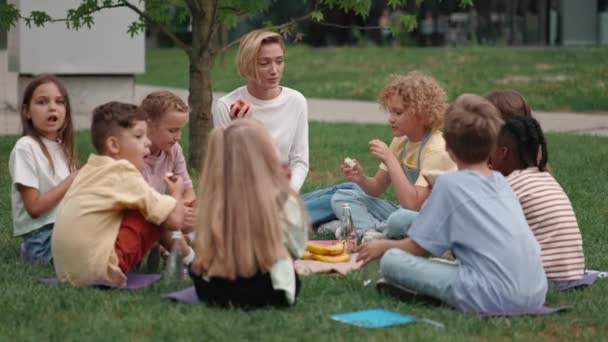 Amistoso profesor almorzando con diversos alumnos al aire libre — Vídeo de stock