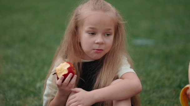 Красивая девушка ест яблоко с одноклассниками на улице — стоковое видео