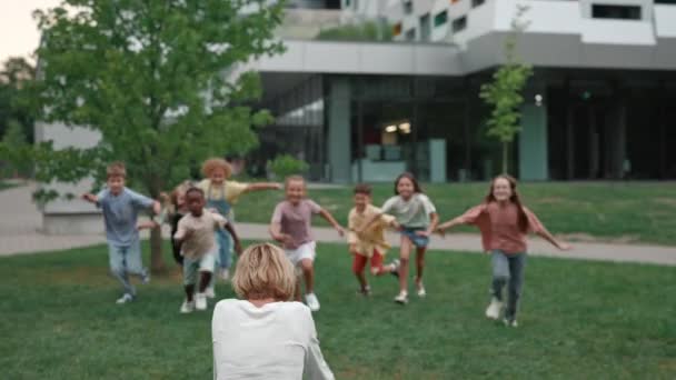 Niños de la escuela mixta abrazando a su profesor favorito al aire libre — Vídeo de stock