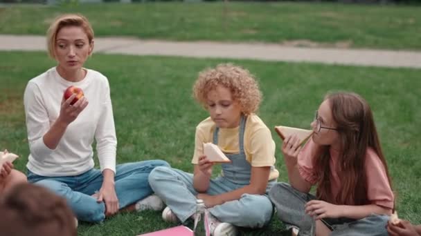 Profesor comiendo comida con clase de niños multirraciales al aire libre — Vídeo de stock