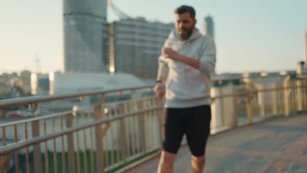 Спортивный бородатый мужчина смотрит на спортивный трекер, который носит под рукой, расслабляясь после бега — стоковое видео