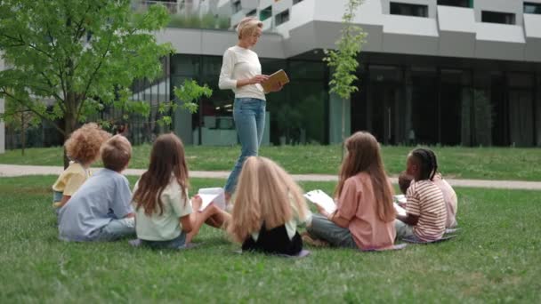 Kvinnlig lärare läser bok för skolbarn utomhus — Stockvideo