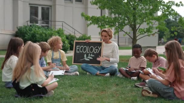 Niños multiétnicos sentados en la hierba durante la lección de ecología — Vídeos de Stock