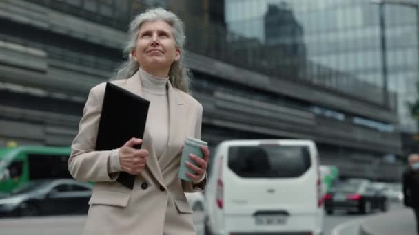 Ładna starsza pani z kawą i schowkiem spaceruje na świeżym powietrzu — Wideo stockowe