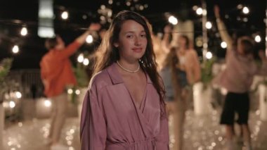 Arkadaşları arkada dans ederken çatıda poz veren bir kadın