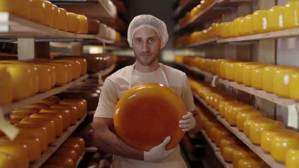 乳制品奶牛场工作时穿着制服的合格奶酪专家的画像 白人男子站在堆放着装满奶酪头的木架的仓库里 — 图库视频影像