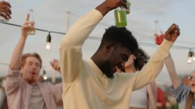 Ellerinde alkollü içki tutan ve çatıda melez ırk arkadaşlarıyla dans eden gülümseyen Afrikalı bir adam. Tasasız insanlar yaz haftasonlarının tadını çıkarıyorlar. Parti zamanı.