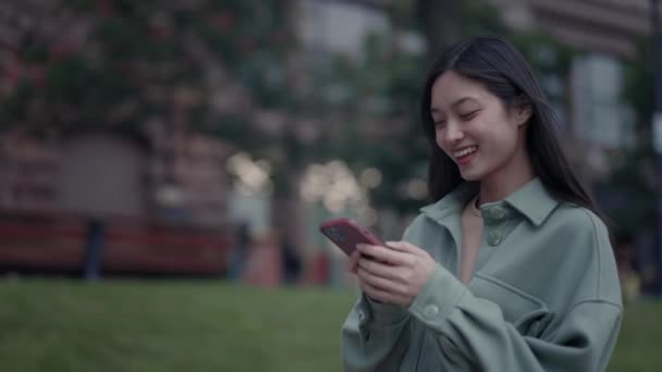 Vidám ázsiai nő sétál az utcán, és használja okostelefon — Stock videók