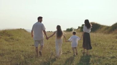 Dört kişilik beyaz bir aile el ele tutuşup doğada yürüyor.