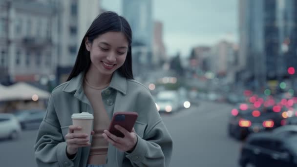 Mujer china sosteniendo teléfono inteligente y taza de café en la calle — Vídeos de Stock