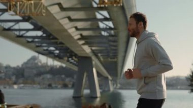 Gri kapüşonlu aktif adam nehir kenarında koşuyor.