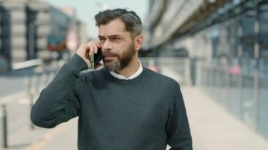 Orta yaşlı işadamı dışarıda cep telefonuyla konuşuyor.