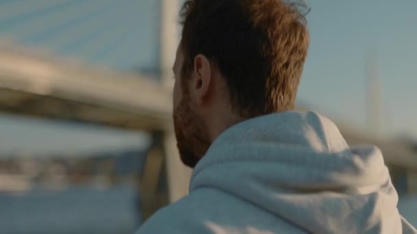 Спортивний чоловік у сірому светрі біжить біля міської річки — стокове відео