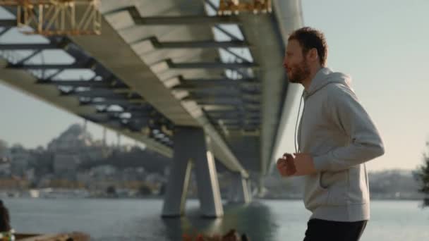 Homme actif en sweat gris jogging près de la rivière de la ville — Video