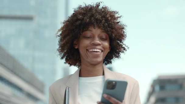 Mujer africana mirando en el móvil y sonriendo al aire libre — Vídeos de Stock