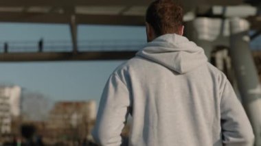 Gri kapüşonlu genç kızıl adam şehir nehrinin yakınlarında koşuyor.