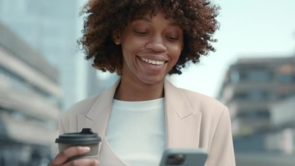 Negro dama sonriendo mientras mirando en mobiel pantalla al aire libre — Vídeos de Stock