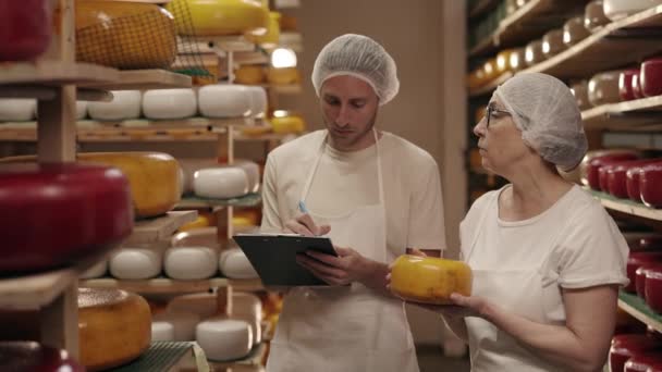 Nő és férfi ellenőrzi a sajt öregedését a tejüzemben — Stock videók