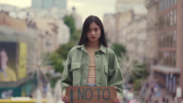 Asiatisk kvinna står på gatan med No to Racism banner — Stockvideo