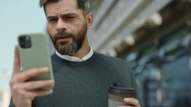 İş adamı elinde kahve ve cep telefonuyla yürüyor.