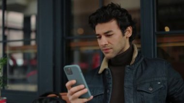 Kafe terasında dinlenirken cep telefonunda mesajlaşan Arap adam.