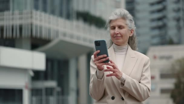 Элегантная пожилая женщина, стоящая на улице и использующая мобильный телефон — стоковое видео