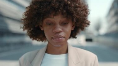 Resmi giyinmiş Afrikalı bir kadın dışarıda kameraya bakıyor.