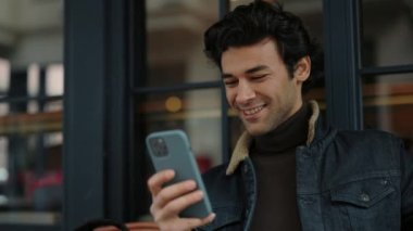 Kafe terasında dinlenirken cep telefonu kullanan gülümseyen Arap adam.