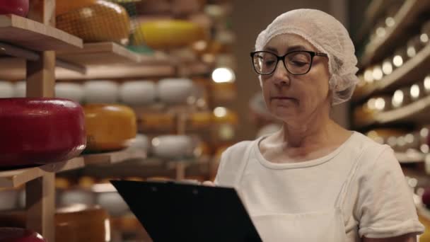 Mature dame écriture sur presse-papiers tout en comptant les têtes de fromage — Video