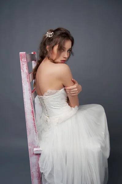 Jonge bruid alleen zitten op een krukje in trouwjurk — Stockfoto
