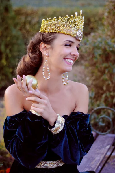 Smiling young woman dressed like queen holding an apple — Stock Photo, Image