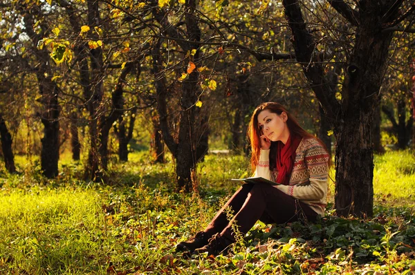 Jeune femme aux longs cheveux roux lisant sous l'arbre — Photo