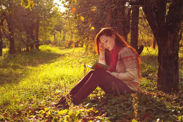 Mujer joven con pelo largo y rojo leyendo bajo el árbol — Foto de Stock