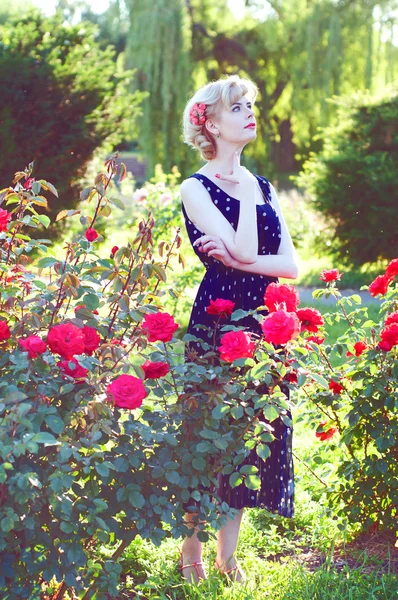 Vakre, blonde kvinne i blå kjole som poserer i hagen – stockfoto
