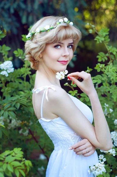 Hermosa mujer rubia en vestido blanco posando en el jardín Imágenes de stock libres de derechos
