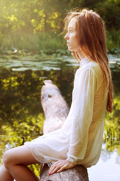 Rude włosy kobieta siedzi na korze drzew, w pobliżu rzeki — Zdjęcie stockowe