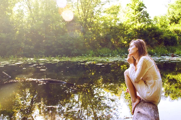 Redhead woman sitting on a tree bark near river — Stock Photo, Image