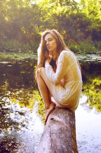 Руда жінка сидить на корі дерева біля річки — стокове фото
