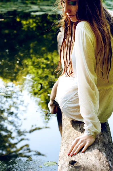 Woman in wet clothes and wet hair sitting on a tree branch near — Stock Photo, Image