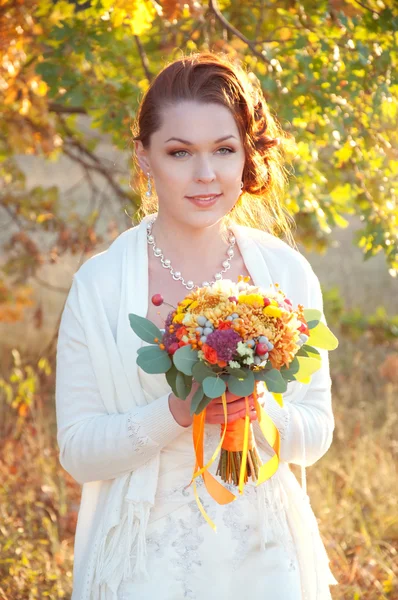 Schöne rothaarige Braut im weißen Kleid mit Herbststrauß — Stockfoto