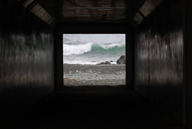 Tünelin karanlığının ötesindeki dalgalı kıyı şeridi.