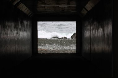 Tünelin karanlığının ötesindeki dalgalı kıyı şeridi.